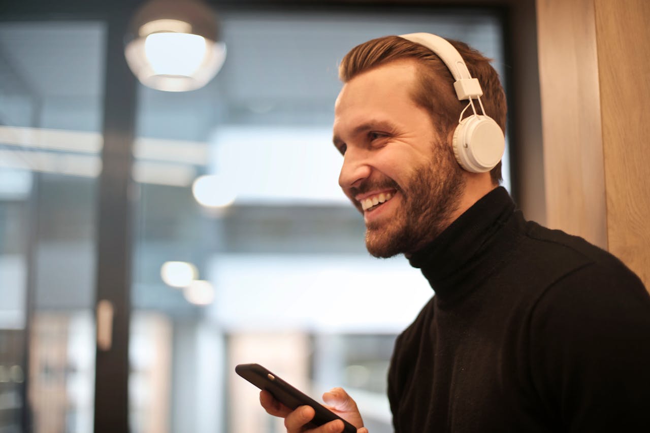 services-05 Bearded man smiling with headphones and smartphone indoors, enjoying music.